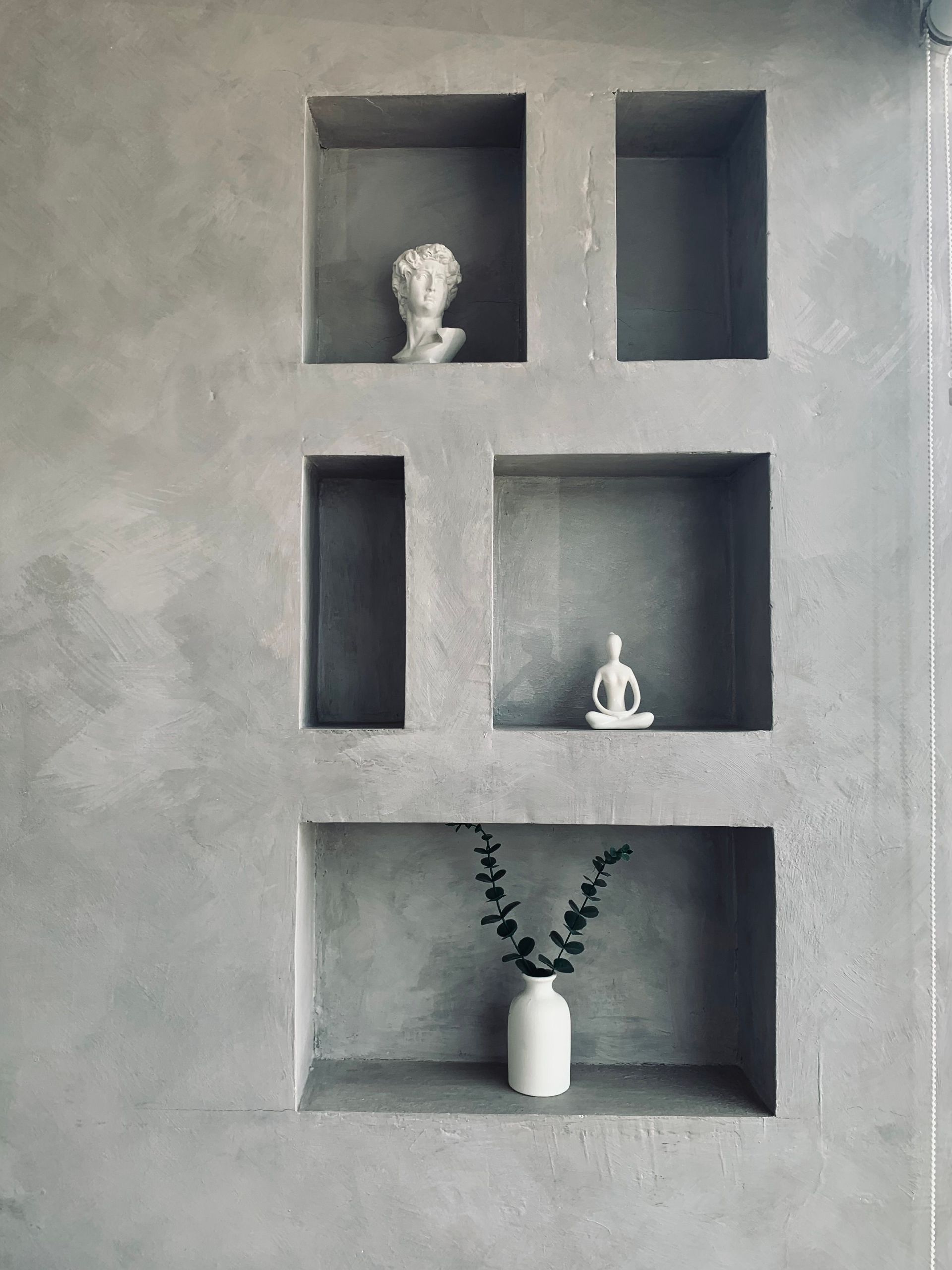 A minimalist wall design featuring decorative figurines and a vase in various niches.