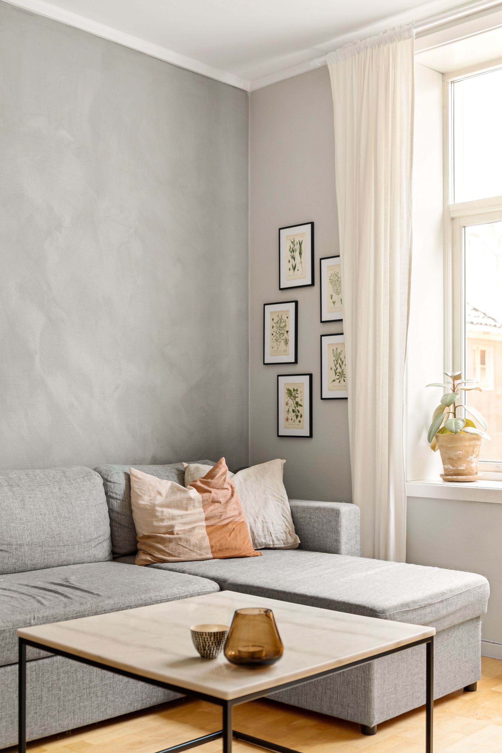 Chic minimalist living room featuring a grey sofa, modern art decor, and large window with natural light.