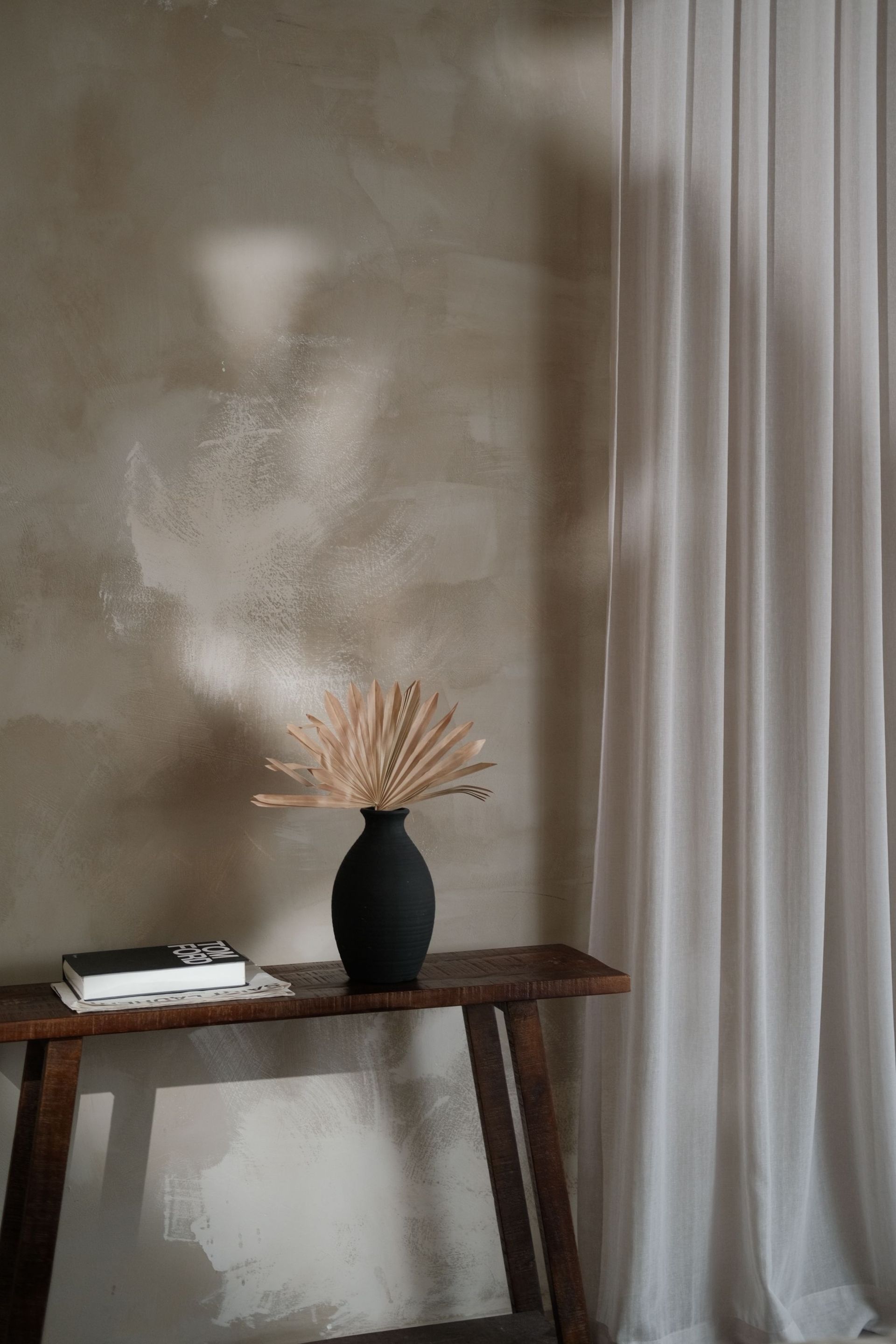 Cozy minimalist interior featuring a black vase with dry flowers on a console table against textured wall.